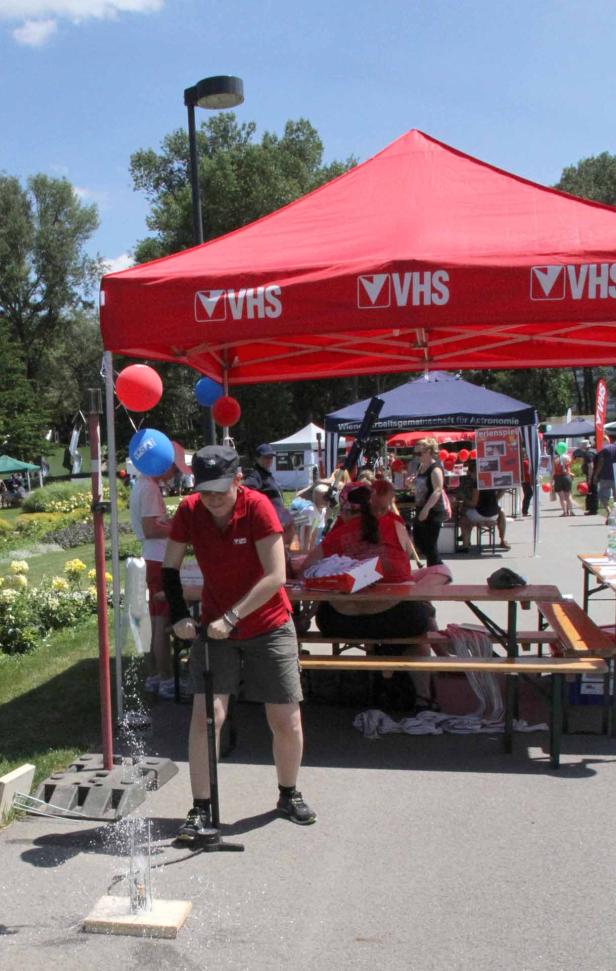 Eine Frau pumpt Wasser an einem Stand der VHS auf einem öffentlichen Platz.