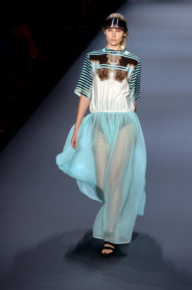 Eine Frau mit einem transparenten Visier und einem hellblauen Kleid auf einem Laufsteg.