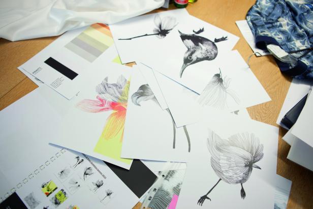 Auf einem Tisch liegen verschiedene Zeichnungen von Blumen und Vögeln sowie Farbmuster.
