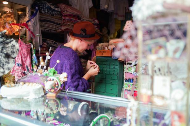 Eine Frau mit Hut arbeitet an einem kleinen, grünen Schrank in einem Laden.
