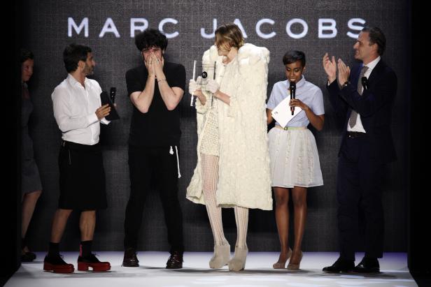 Eine Frau im weißen Mantel erhält eine Auszeichnung auf einer Bühne mit Zuschauern.