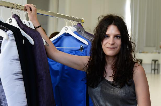 Eine Frau steht vor einer Kleiderstange mit verschiedenen Kleidungsstücken.