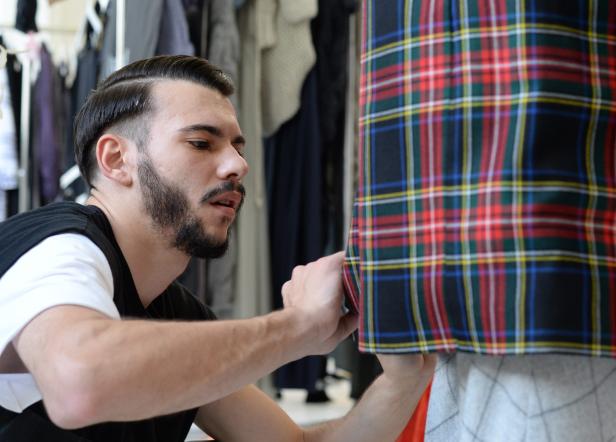 Ein Mann befestigt ein kariertes Stoffmuster an einer Schneiderpuppe.