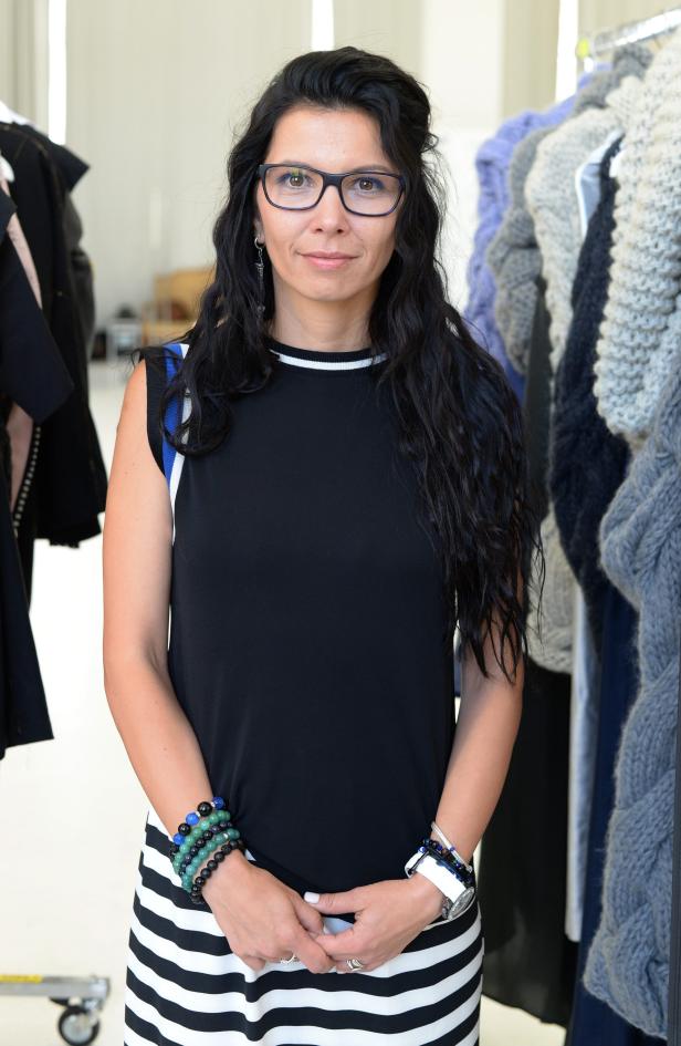 Eine Frau mit Brille, schwarzem Oberteil und gestreiftem Rock steht vor einem Kleiderständer.