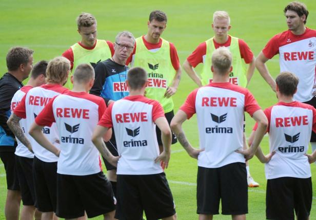 Ein Trainer spricht zu einer Gruppe von Fußballspielern auf einem grünen Rasen.