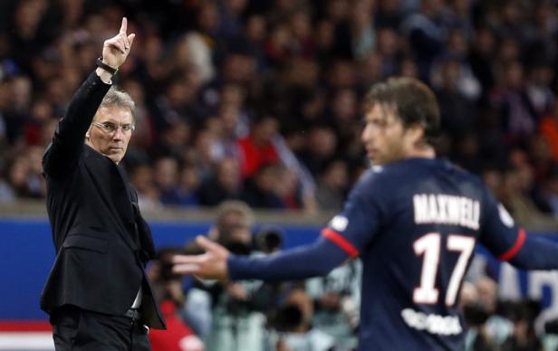 Ein Trainer gestikuliert während eines Fußballspiels, während der Spieler Maxwell mit der Nummer 17 im Hintergrund steht.