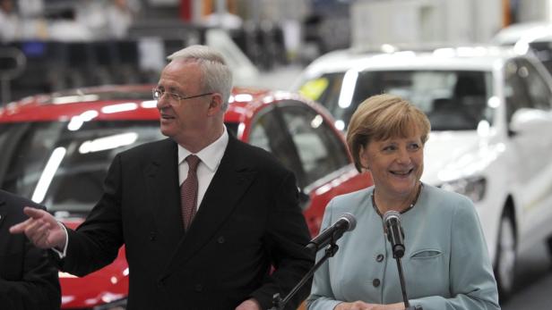 Angela Merkel und ein Mann stehen vor Autos in einer Fabrikhalle.