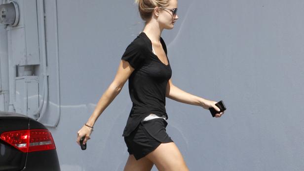 Eine Frau mit Sonnenbrille geht mit einem Handy in der Hand die Straße entlang.