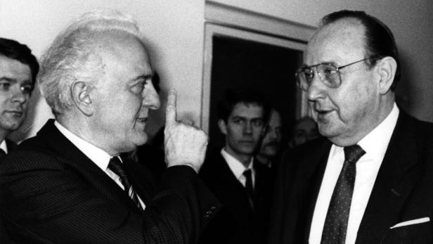 Ein Schwarzweißfoto von zwei Männern in Anzügen, einer mit erhobenem Zeigefinger.