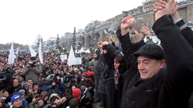 Eine Menschenmenge demonstriert mit erhobenen Händen und Transparenten in einer verschneiten Stadt.
