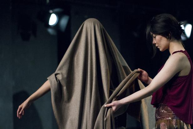 Eine Frau drapiert ein großes Tuch über eine andere Person.