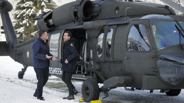 Zwei Männer stehen vor einem schwarzen Hubschrauber auf einer schneebedeckten Fläche.