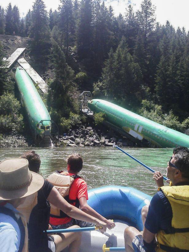 Eine Gruppe von Menschen raftet auf einem Fluss an zwei Flugzeugrümpfen vorbei.