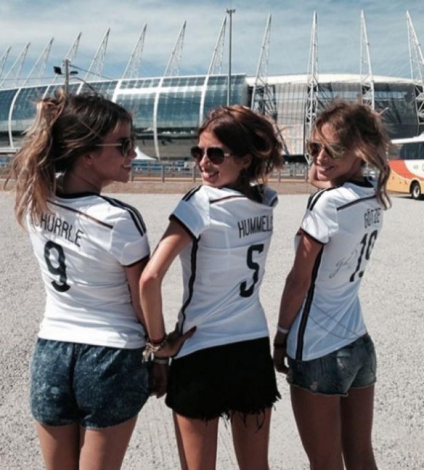 Drei junge Frauen in Deutschland-Trikots posieren vor einem Fußballstadion.