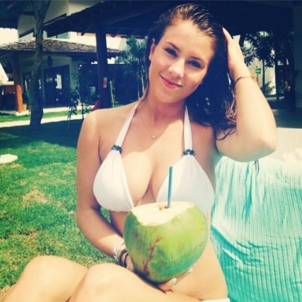 Eine junge Frau im Bikini hält eine Kokosnuss mit Strohhalm in der Hand.