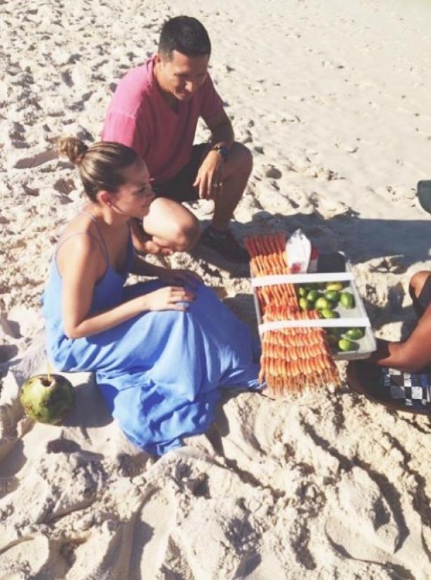 Ein Mann und eine Frau sitzen am Strand neben einem Verkäufer von Garnelen und Limetten.
