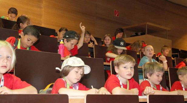 Eine Gruppe von Kindern sitzt in einem Hörsaal und passt auf.