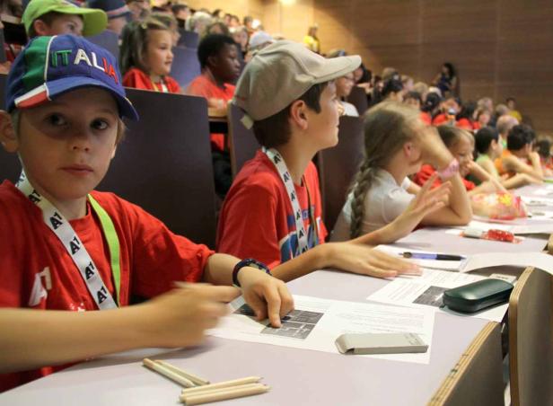 Kinder sitzen in einem Hörsaal und bearbeiten Arbeitsblätter.