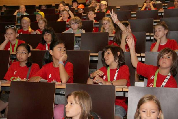 Eine Gruppe Kinder sitzt in einem Hörsaal und hört aufmerksam zu.
