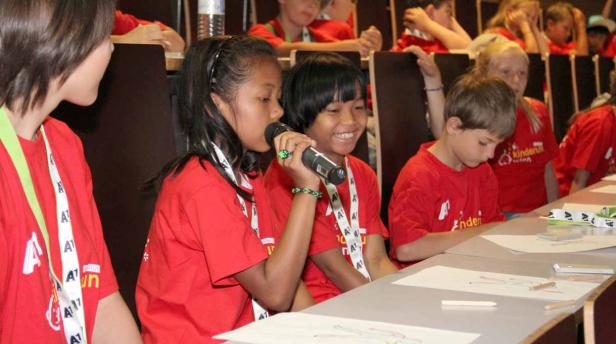 Zwei Kinder sprechen bei einer Veranstaltung ins Mikrofon, während andere zeichnen.
