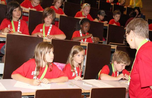 Eine Gruppe von Kindern sitzt in einem Hörsaal und arbeitet an ihren Tischen.