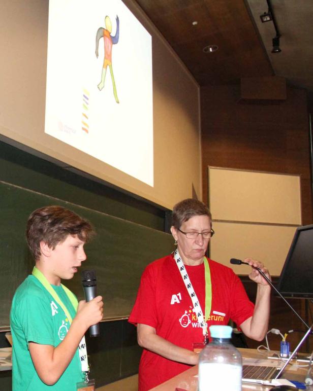 Ein Junge präsentiert neben einer Frau ein farbiges Diagramm auf einer Leinwand.