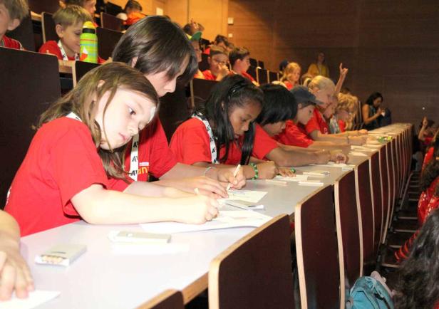 Eine Gruppe Kinder sitzt in einem Hörsaal und zeichnet.