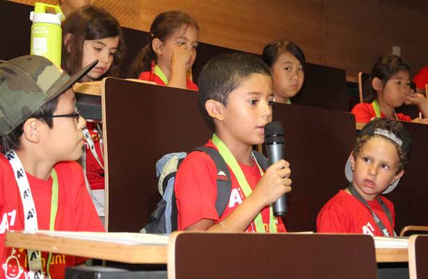 Ein Junge spricht in ein Mikrofon vor einer Gruppe von Kindern.