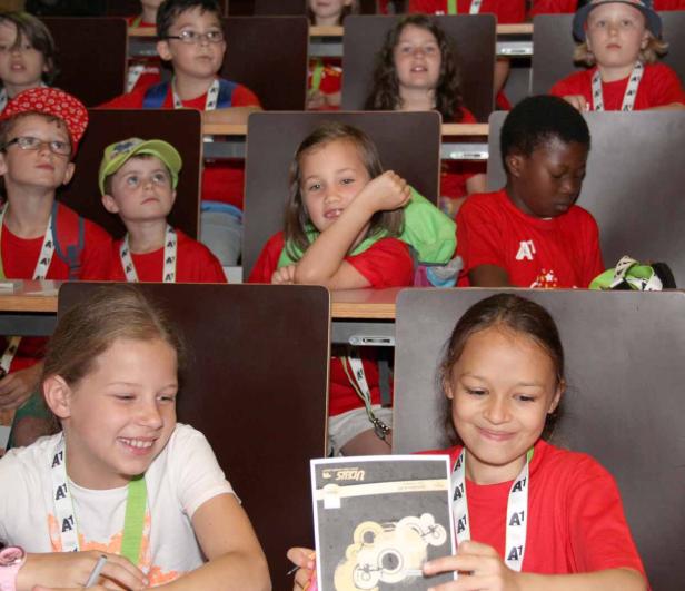 Eine Gruppe von Kindern sitzt in einem Hörsaal an ihren Tischen.