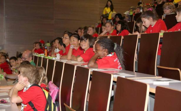 Eine Gruppe von Kindern sitzt in einem Hörsaal und hört aufmerksam zu.