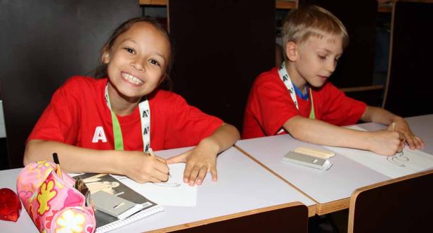 Zwei Kinder sitzen an Tischen und zeichnen auf Papier.