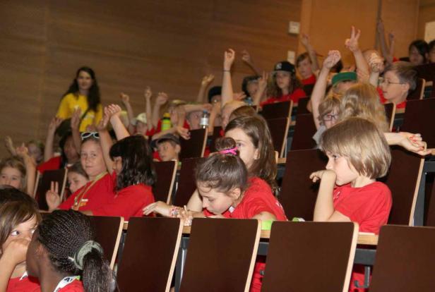 Eine Gruppe Kinder sitzt in einem Auditorium und meldet sich.