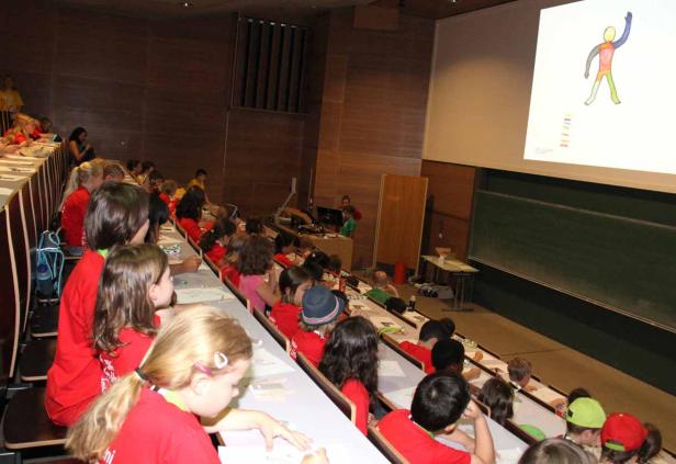 Kinder sitzen in einem Hörsaal und schauen auf eine Präsentation.