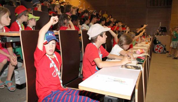 Kinder sitzen in einem Hörsaal und melden sich während einer Veranstaltung.