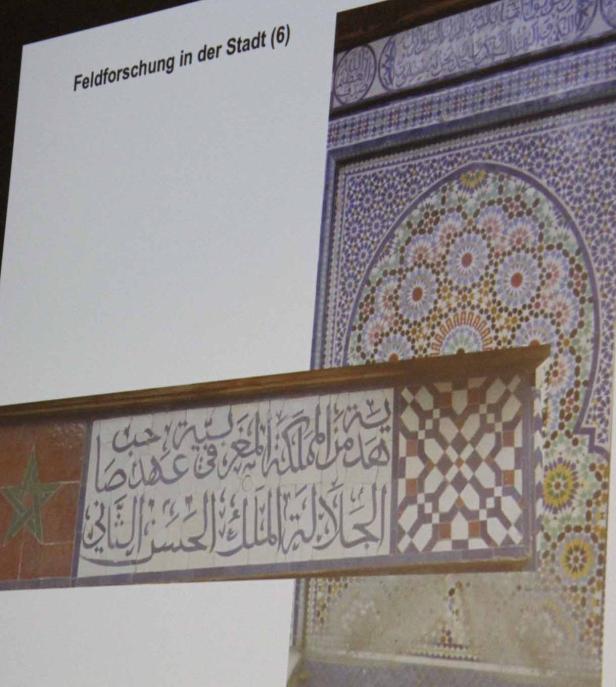 Detailansicht einer Wand mit Mosaiken und arabischer Schrift.