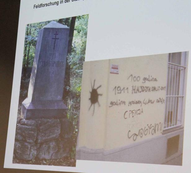 Ein serbischer Grabstein und eine Wand mit Graffiti, darunter die Aufschrift „СРБИЈА“ (Serbien).