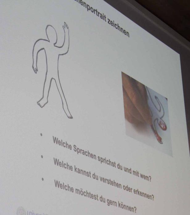 Eine Präsentation zeigt eine Strichmännchen-Zeichnung und Fragen zu Sprachen.