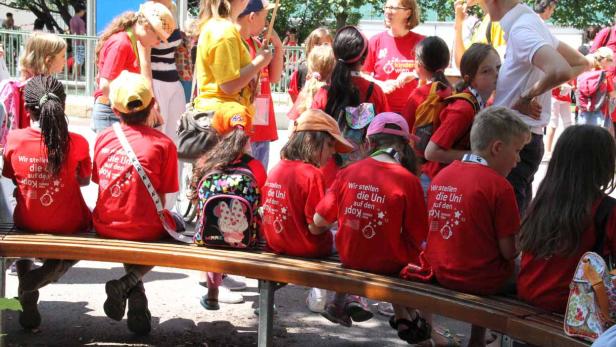 Eine Gruppe Kinder sitzt auf einer Bank und trägt rote T-Shirts.