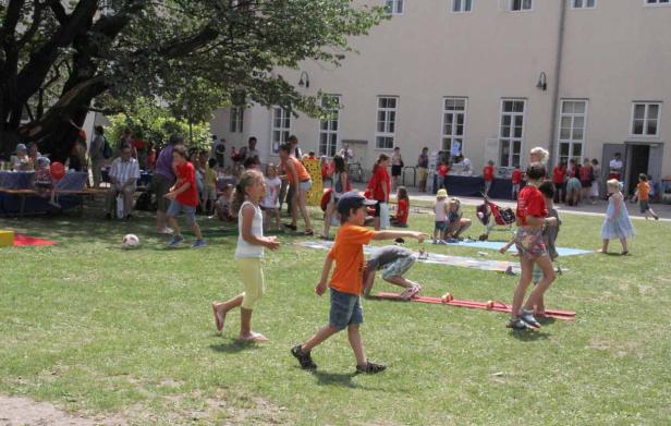 Eine Gruppe Kinder spielt und tobt auf einer Wiese vor einem Gebäude.
