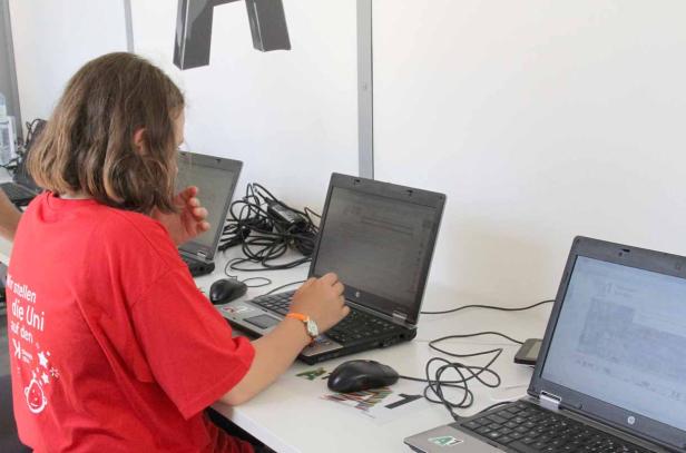 Eine junge Person sitzt an einem Tisch mit mehreren Laptops.