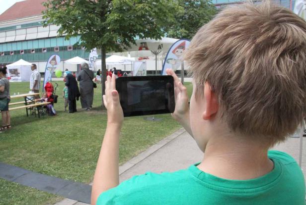 Ein Junge fotografiert mit einem Tablet eine Veranstaltung im Freien.