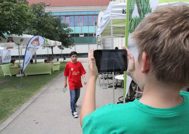 Ein Junge fotografiert einen anderen Jungen mit einem Tablet im Freien.