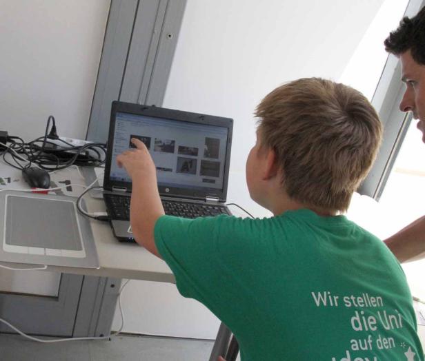 Ein Junge zeigt auf einen Laptop-Bildschirm, während ein Mann daneben steht.