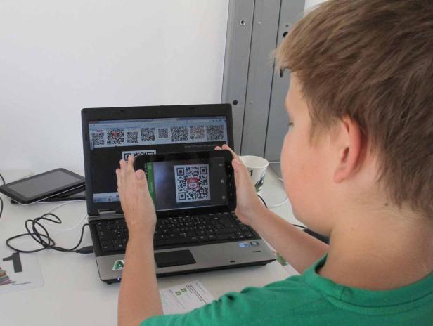 Ein Junge scannt mit einem Tablet einen QR-Code, der auf einem Laptop-Bildschirm angezeigt wird.