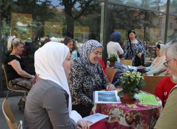 Frauen mit Kopftüchern sitzen an Tischen im Freien und betrachten Bilder.