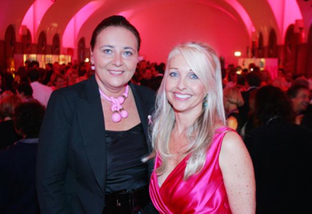 Zwei Frauen posieren auf einer Veranstaltung mit rosa Beleuchtung.