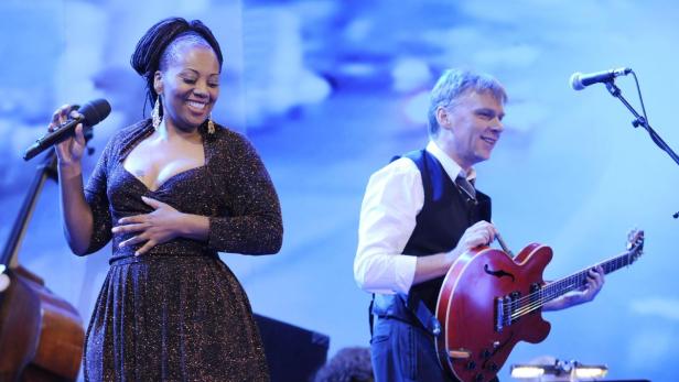 Eine Sängerin mit Mikrofon und ein Gitarrist treten auf einer Bühne auf.