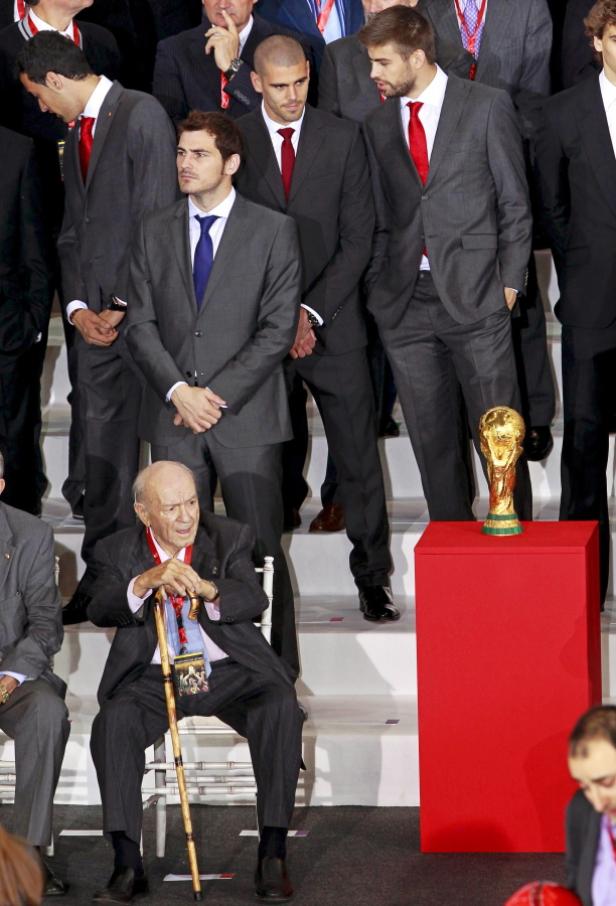 Eine Gruppe von Männern in Anzügen steht um die FIFA-Weltmeisterschaftstrophäe.