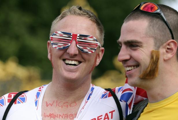 Zwei Wiggins-Wannabees in London Zwei Männer, einer mit Union-Jack-Brille und aufgemaltem „Wiggo Wannabe“ Schriftzug, lächeln.