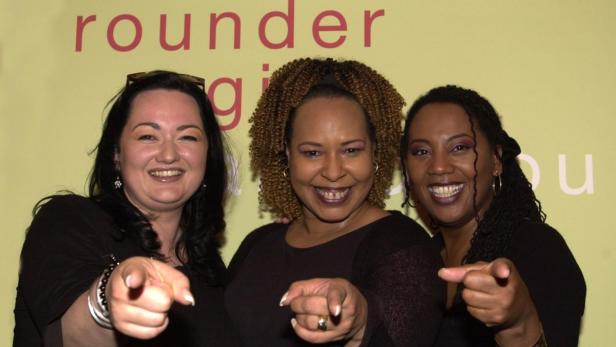 Die drei lächelnden Sängerinnen der Rounder Girls zeigen mit dem Finger auf den Betrachter.